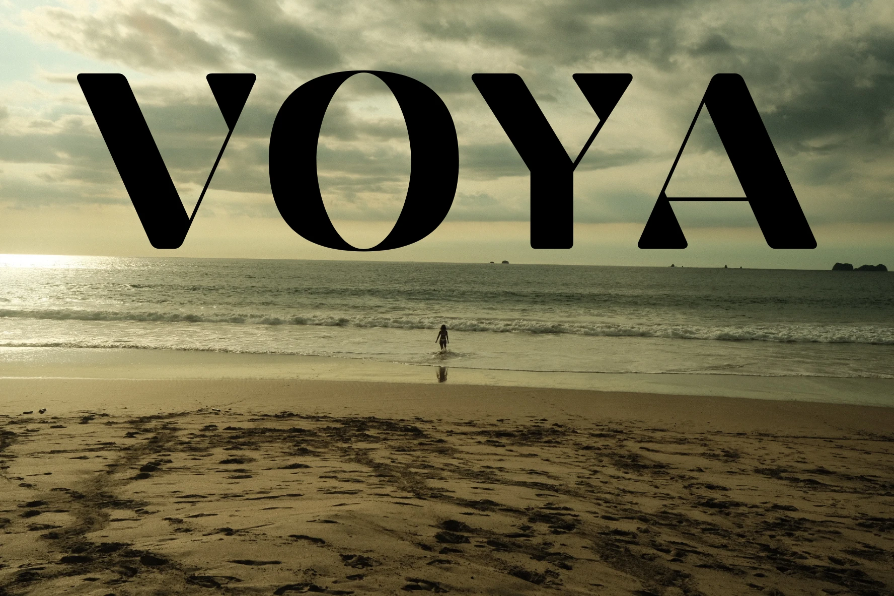 Una persona entra al mar en una playa del Pacífico al atardecer, bajo el logotipo VOYA